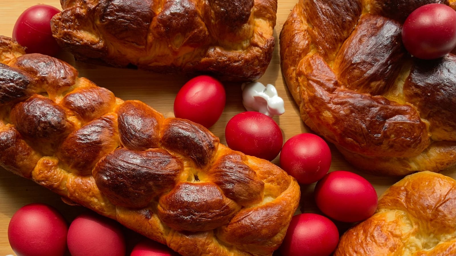 Braided tsoureki loaves surrounded by red-dyed Easter eggs on a wooden surface.