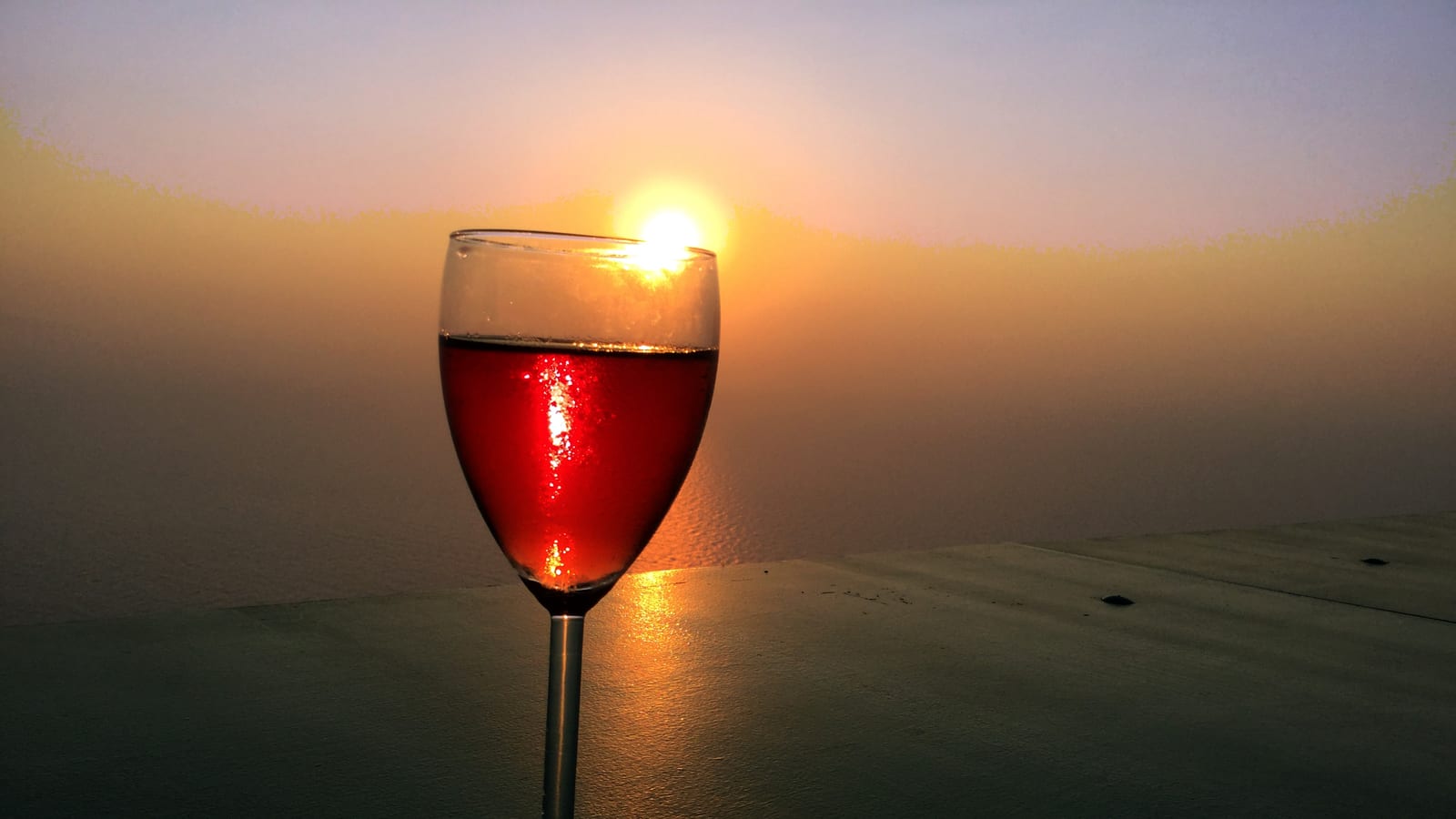 A glass of red wine backlit by the sunset over the sea at a winery on Sikinos, a Greek Cycladic island.