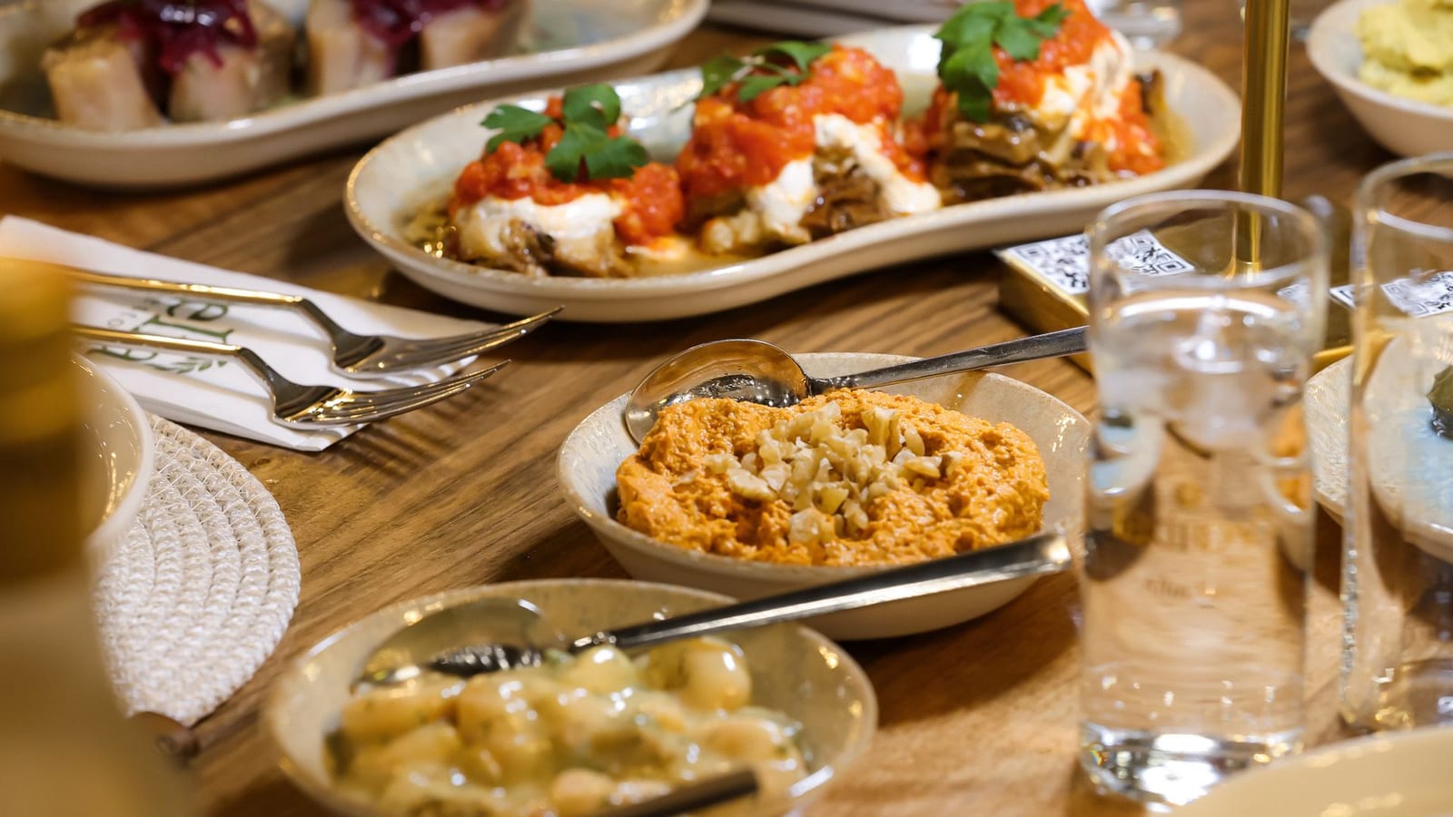 A wooden table spread with Greek meze dishes including dips and stuffed vegetables.