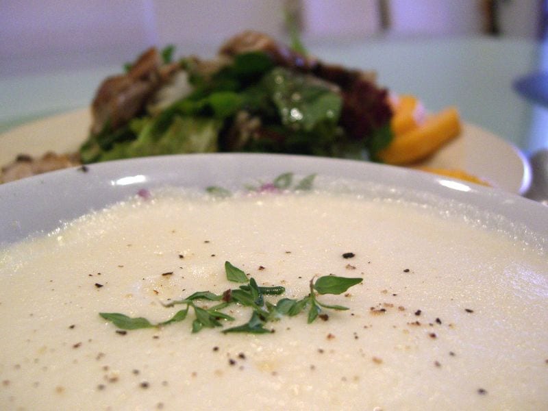 A bowl of pale, creamy avgolemono soup garnished with fresh herbs.
