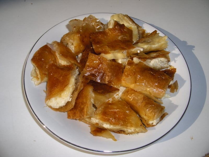 Torn pieces of bougatsa on a plate, showing flaky golden phyllo layers around a soft cheese filling.