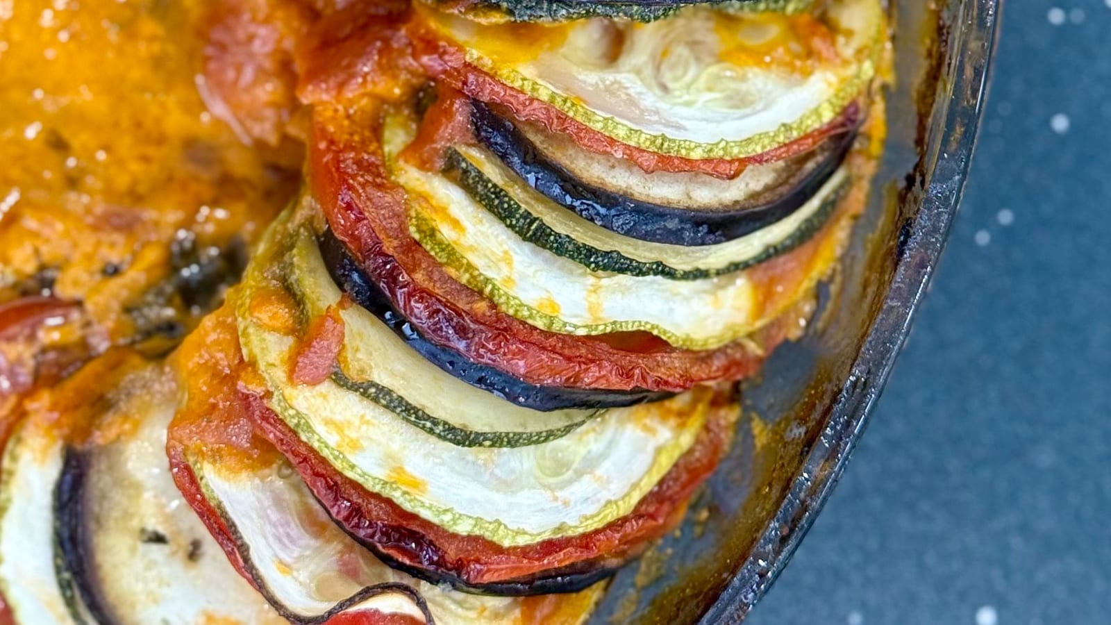 Layered roasted zucchini, eggplant, and tomato in a glossy tomato sauce.