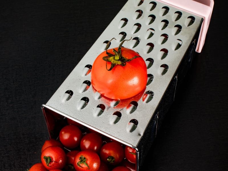 Ripe tomatoes spilling out of a box grater, ready to be grated over a barley rusk.