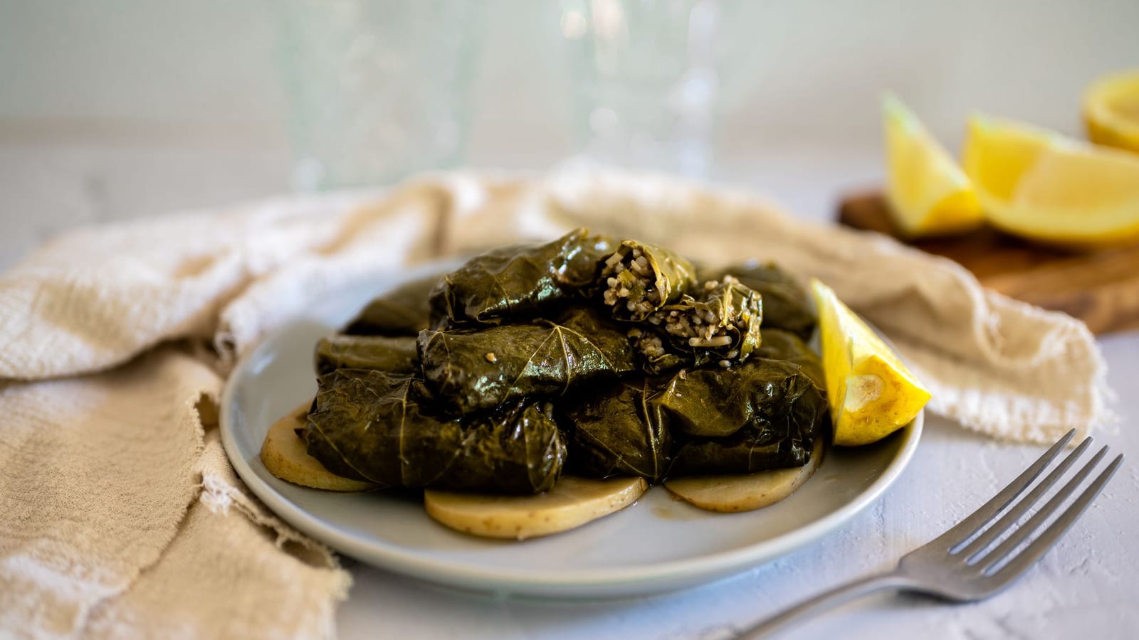 Limon dilimi, keten peçete ve çatalla bir tabakta yığılmış dolma yaprağı sarmaları.