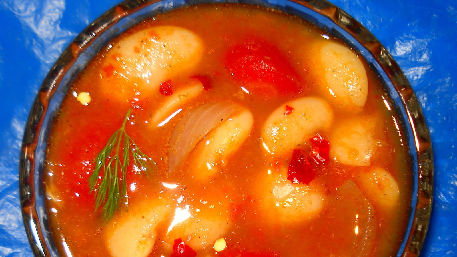 Overhead view of a bowl of fasolada, white bean soup in a rich tomato broth garnished with fresh dill.