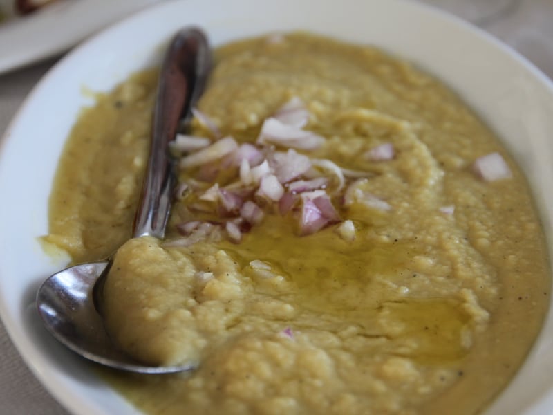 A close-up of fava puree topped with diced onion and olive oil, showing its smooth texture.