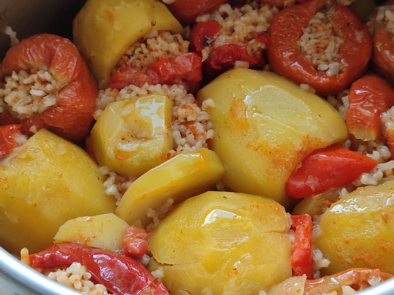 Close-up of hollowed tomatoes and peppers filled with herbed rice before baking.