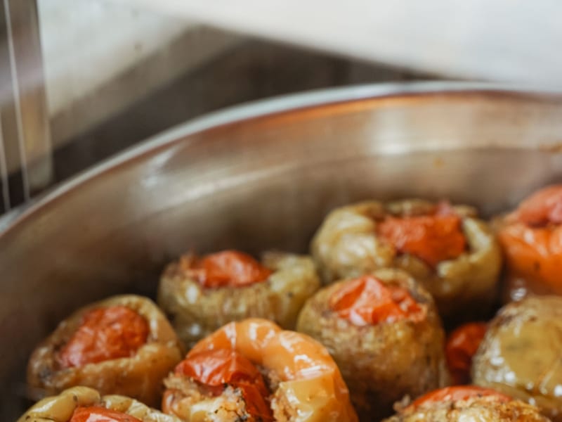 A wide metal pan of freshly baked gemista, stuffed tomatoes and peppers with caramelized skins.