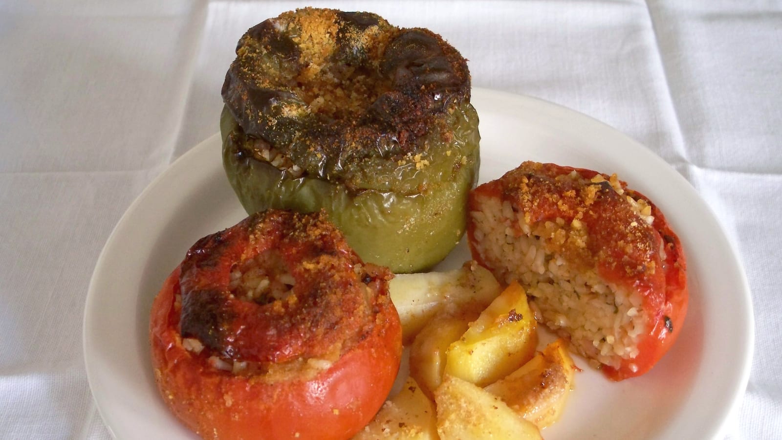 A plate of gemista, stuffed tomatoes and a stuffed green pepper filled with herbed rice, served with roasted potato wedges.