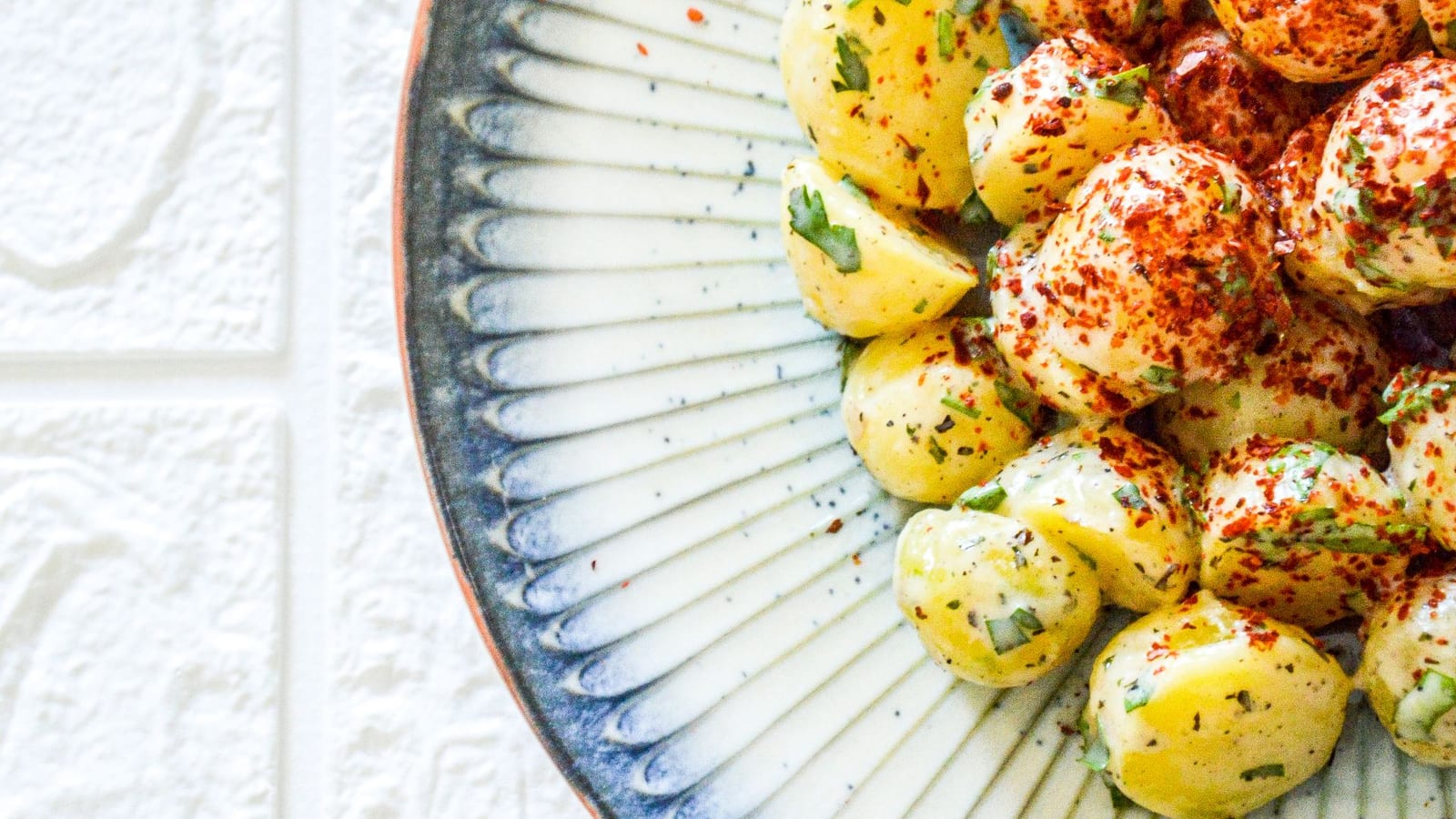 Baby potatoes tossed with herbs and spices on a blue-patterned ceramic plate.
