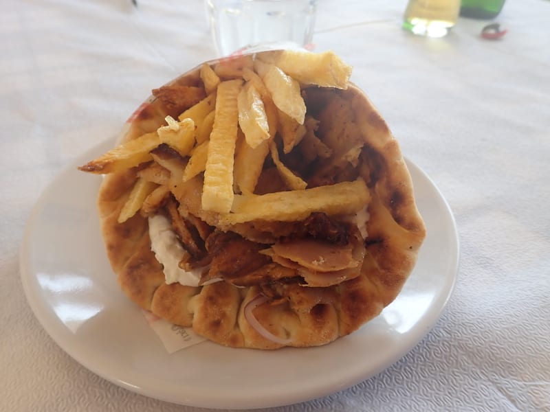 Dilimlenmiş etle, patates kızartmasıyla, domates ve soğanla doldurulmuş açık bir gyro pita, bir tabakta servis edilmiş.