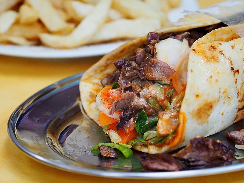A wrapped gyro pita cut open, showing layers of meat, tomato, onion, and sauce inside.