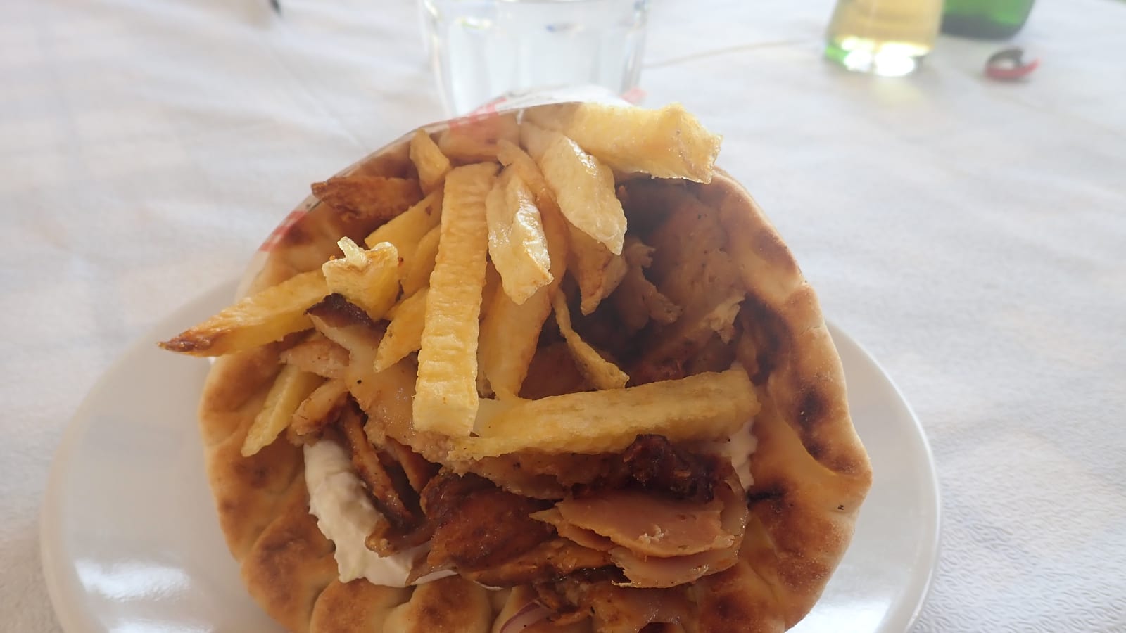 An open-faced gyro pita piled high with sliced meat, fries, tomato, and onion, served on a plate.
