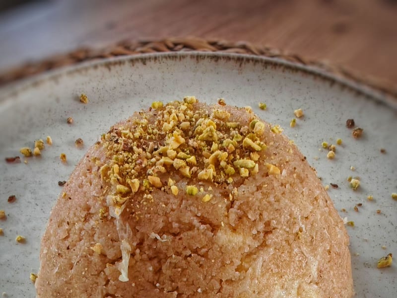 Üzeri dövülmüş fıstıkla süslenmiş, seramik bir tabakta kubbe şeklinde irmik helvası.