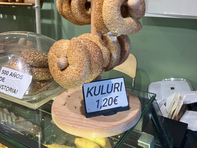 Sesame-crusted koulouri rings hanging on a wooden bakery display rack, priced at 1.20 euros each.