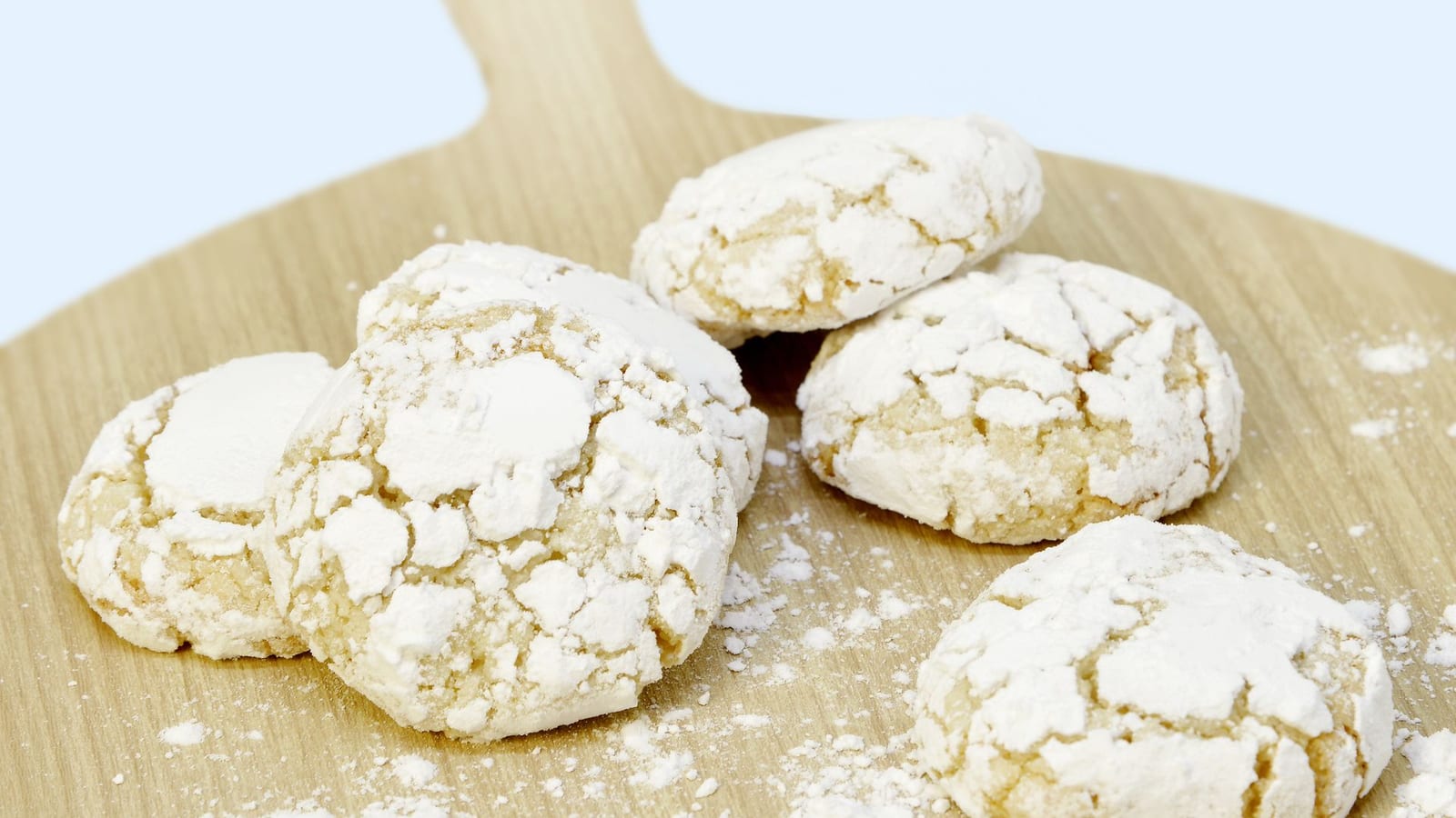 Round shortbread cookies thickly dusted with powdered sugar on a wooden board.