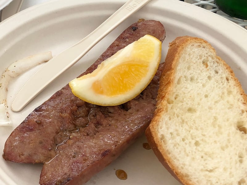 A close view of grilled loukaniko sausage with a lemon wedge and a slice of bread.