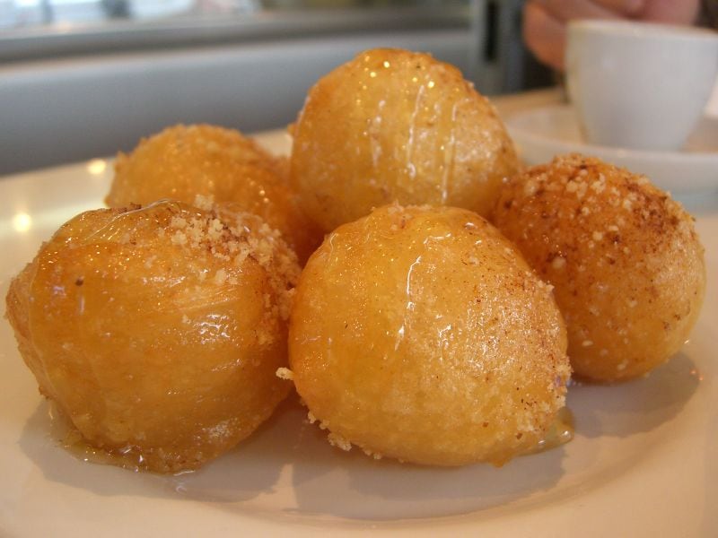 A plate of loukoumades, deep-fried Greek honey puffs, glossy with syrup.