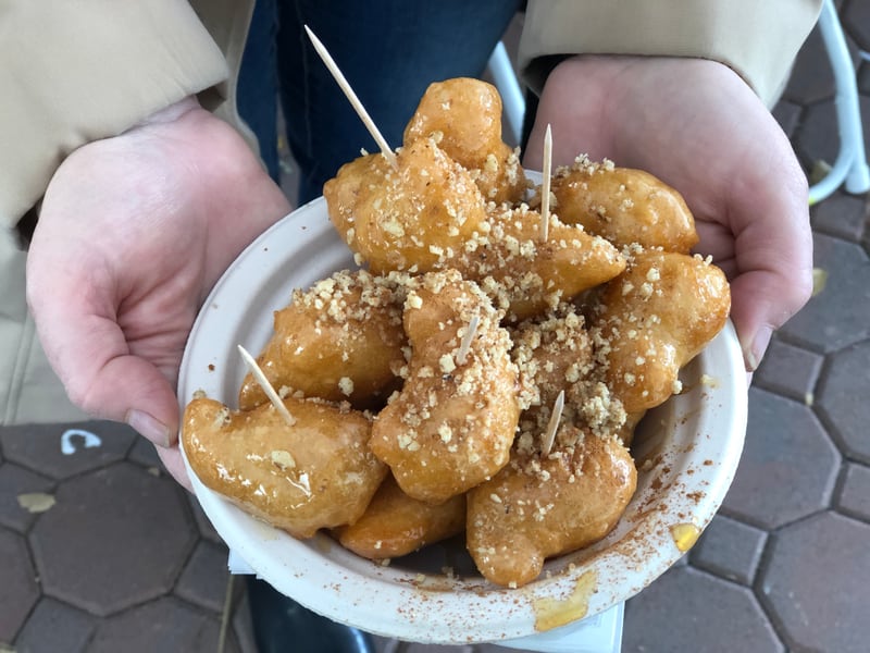 A bowl of loukoumades topped with crushed walnuts and cinnamon, served with toothpicks at a festival stand.