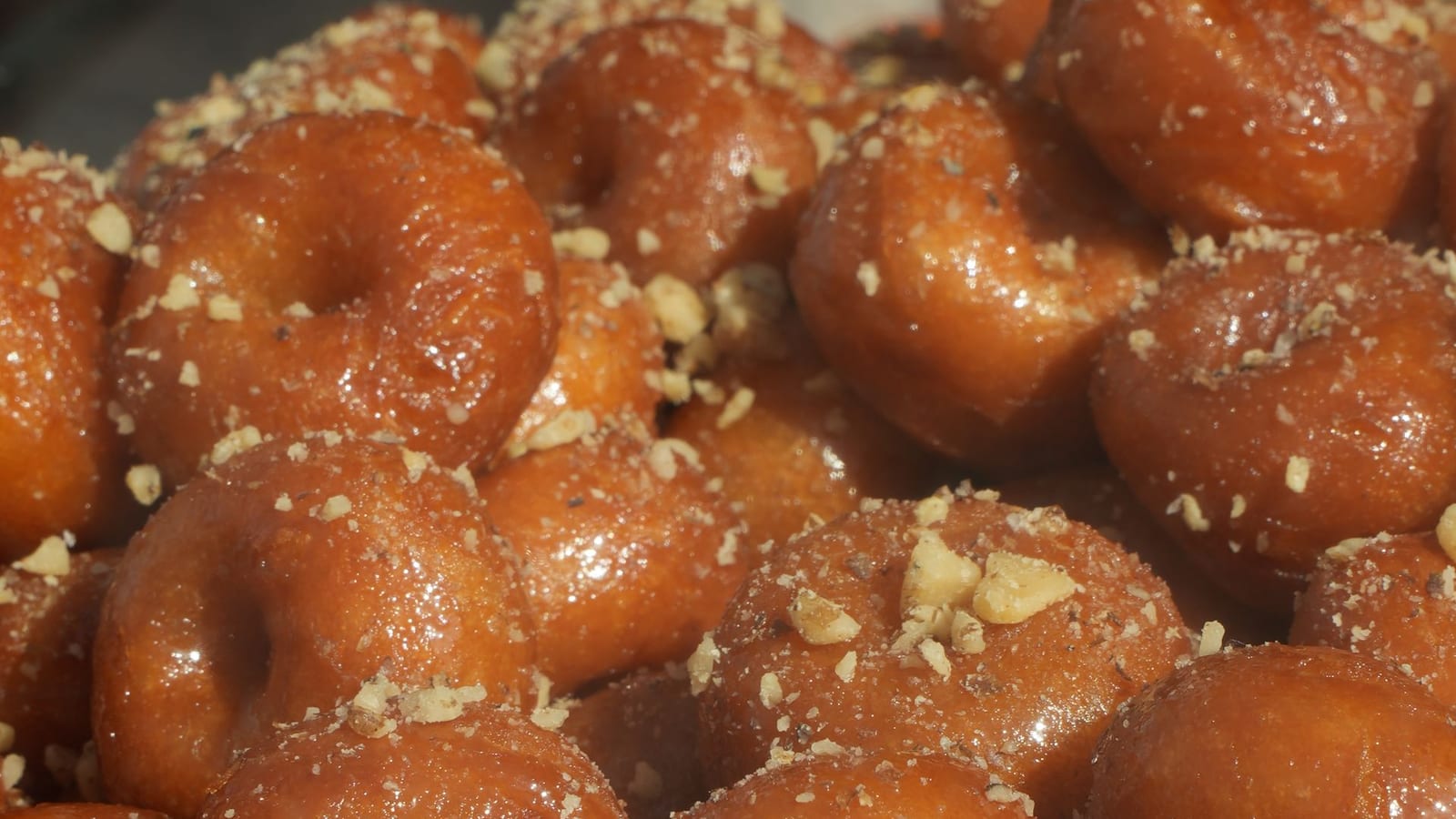 A pile of golden fried dough balls glazed in honey syrup and sprinkled with chopped walnuts.