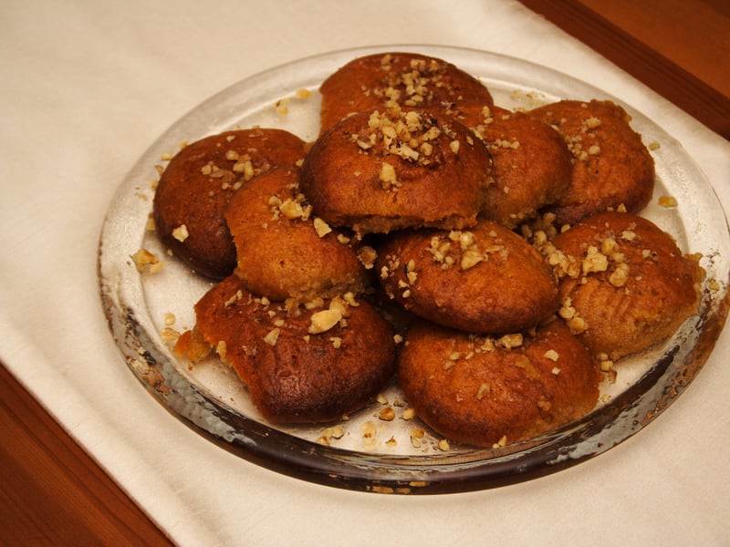 A plate of melomakarona topped with crushed walnuts, stacked and glossy with syrup.