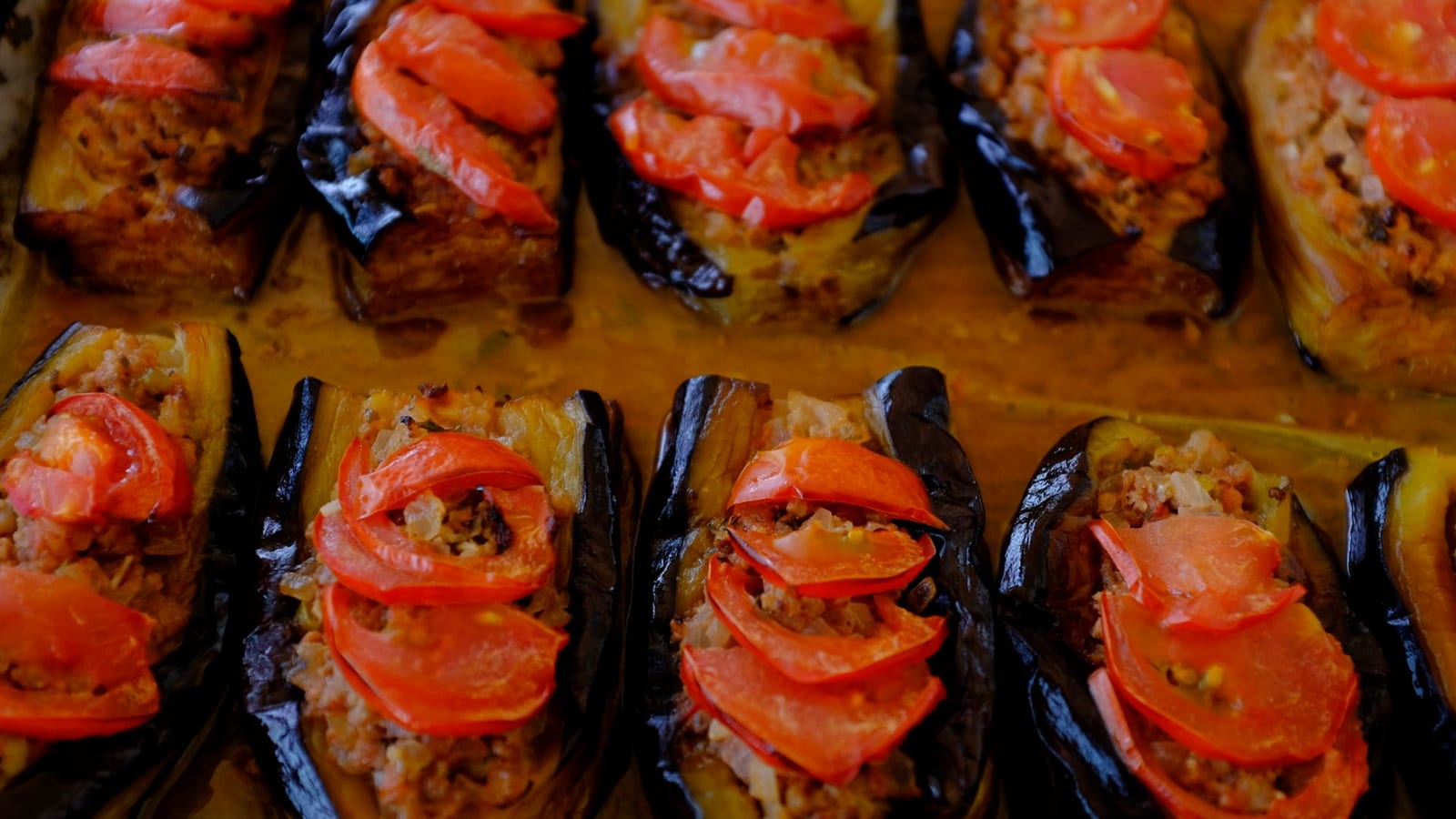 A tray of halved stuffed eggplants topped with meat filling and tomato slices.