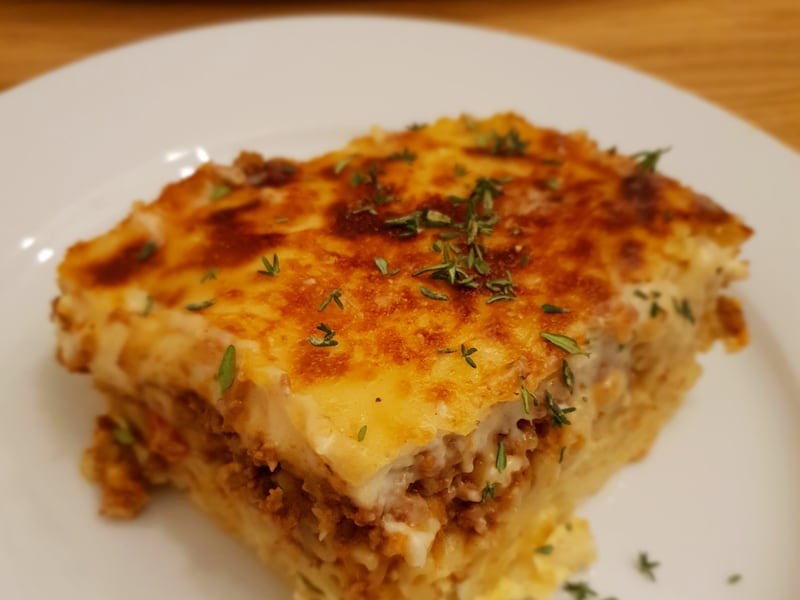 A plated slice of pastitsio showing the golden baked béchamel topping over layers of pasta and meat sauce.