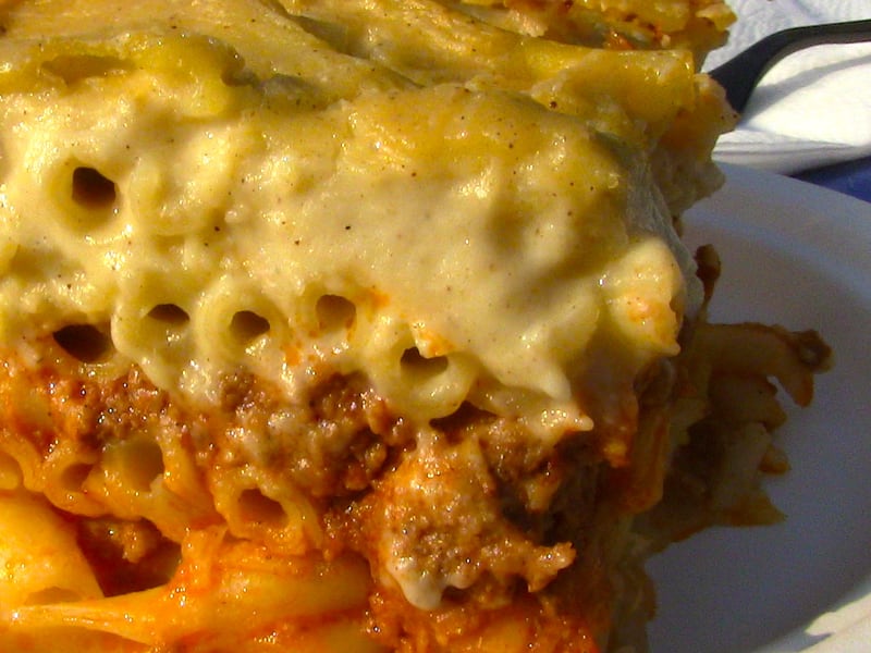 A close-up cross-section of pastitsio showing the tube pasta, meat sauce, and béchamel layers.