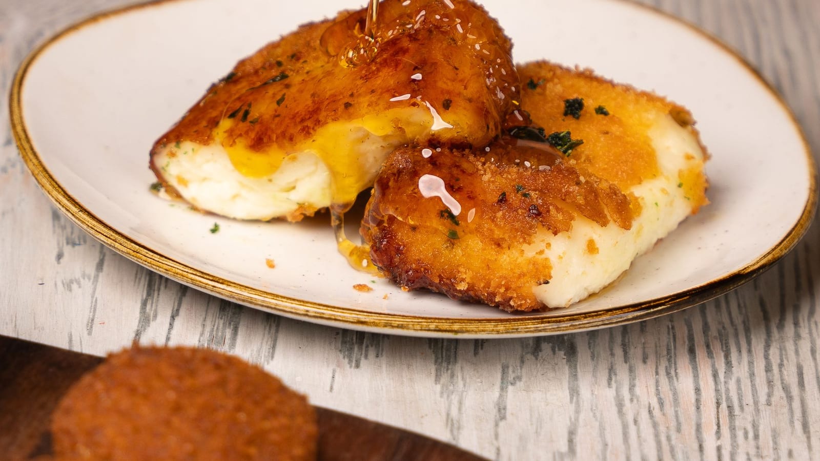 Golden fried cheese slices drizzled with honey on a white plate.