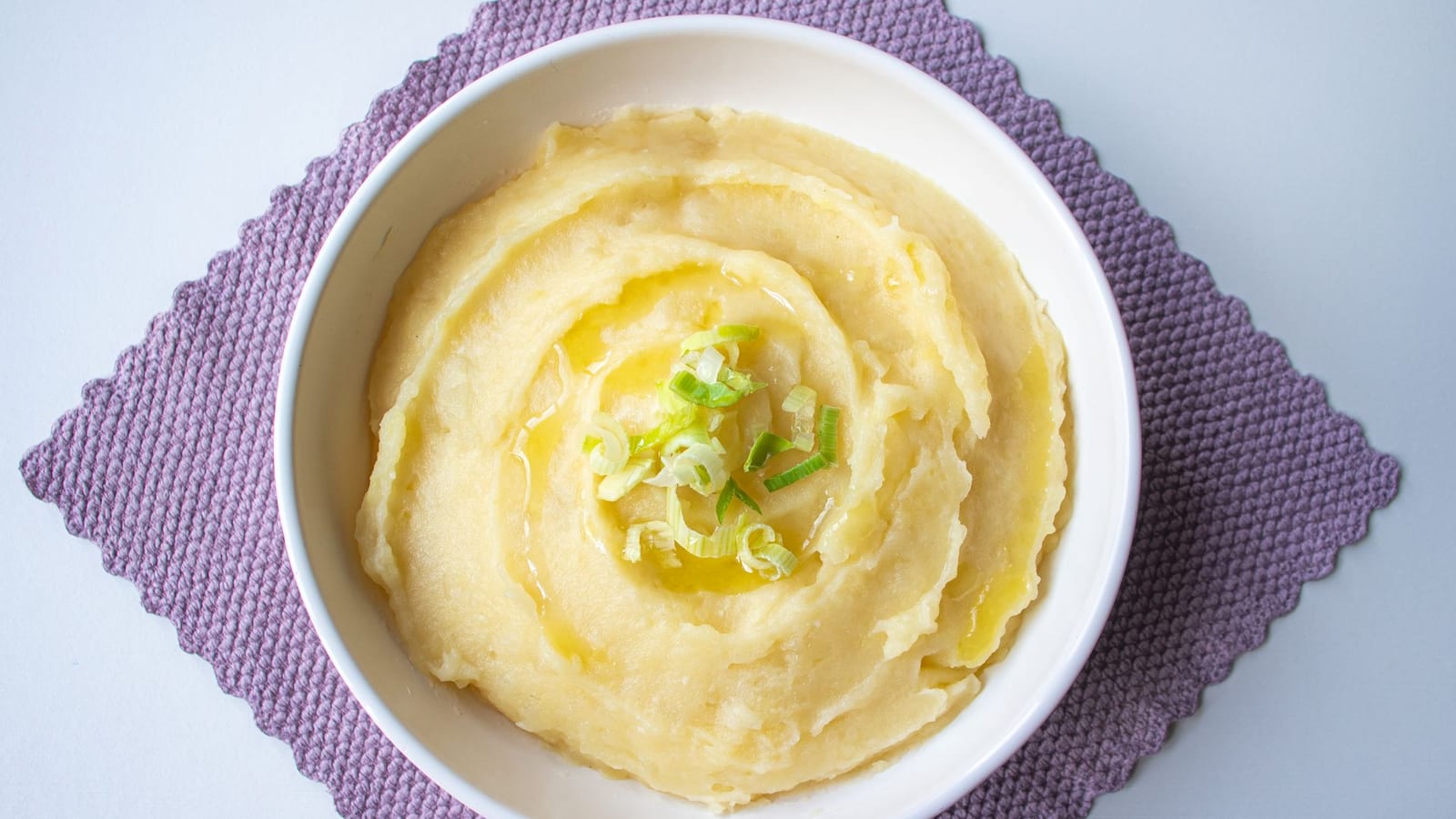 A swirl of creamy mashed potato dip drizzled with olive oil and scallions in a white bowl.