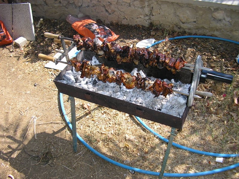 Souvlaki skewers roasting over charcoal on an outdoor rotisserie grill.