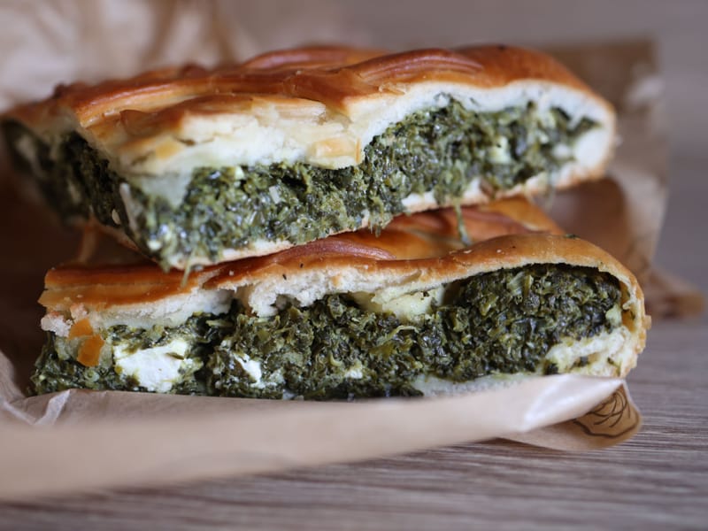 Cross-section of baked spanakopita showing the green spinach and feta filling inside a golden pastry crust.
