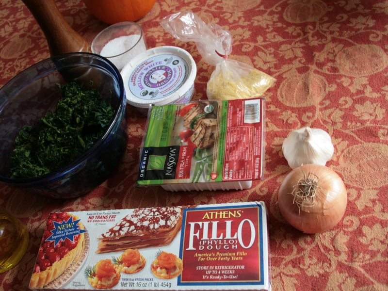 Spanakopita ingredients laid out: chopped spinach, feta, phyllo dough, onion, and garlic.