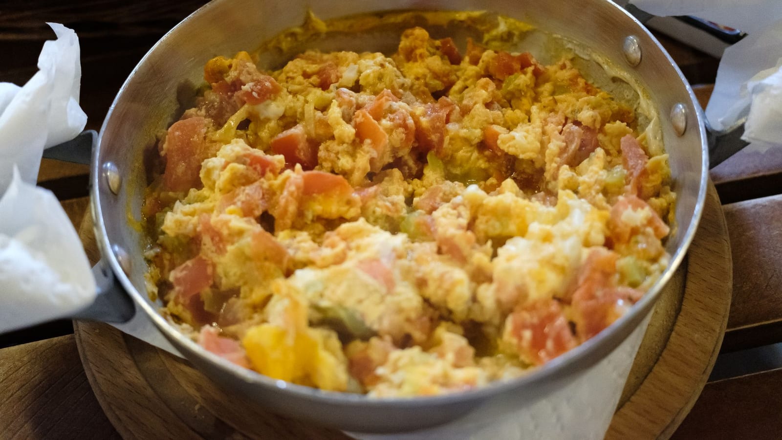 Scrambled eggs cooked with tomato in a metal pan.