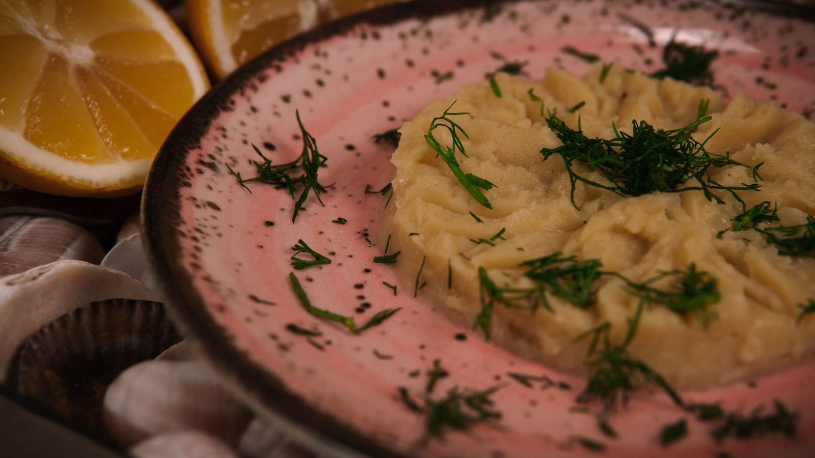 A pale whipped dip on a pink ceramic plate garnished with fresh dill and lemon.